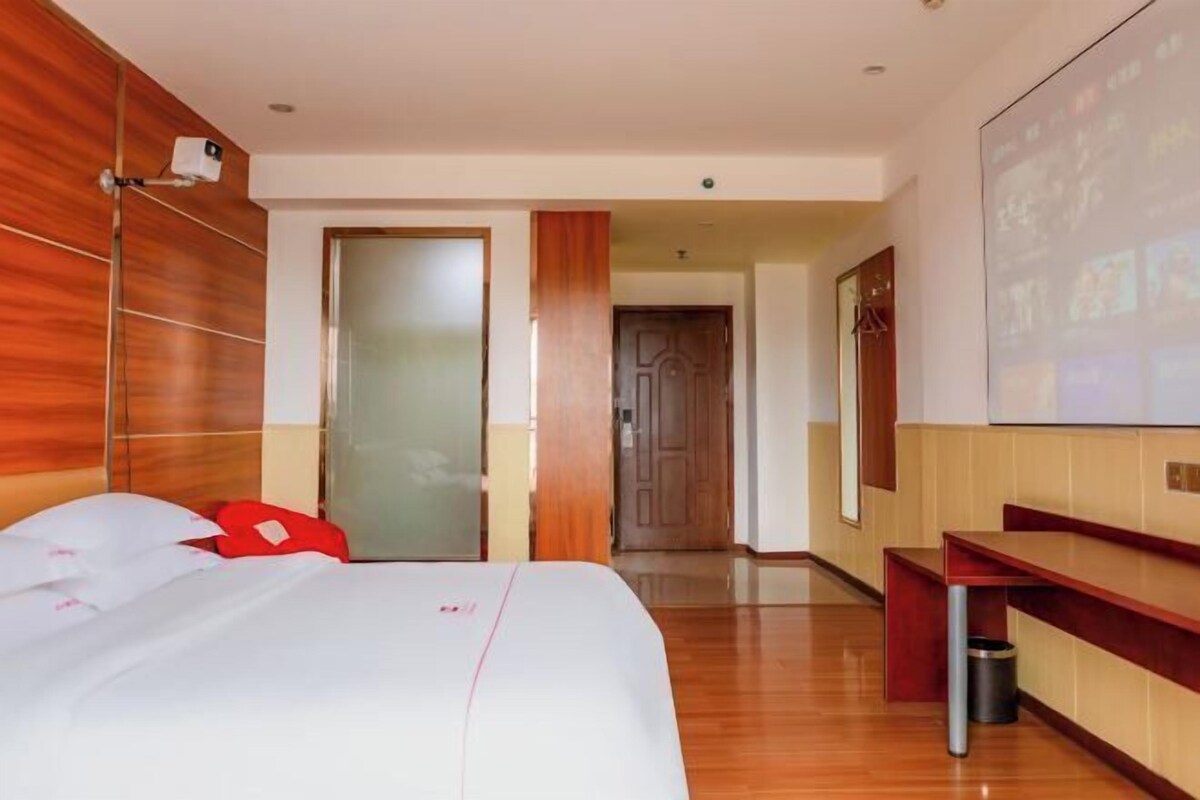 A hotel room with a bed, a desk, a trash bin, and a projection screen on the wall.