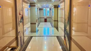 Corridoio d'albergo con pavimento riflettente, opere d'arte incorniciate alle pareti e un cestino centrale.