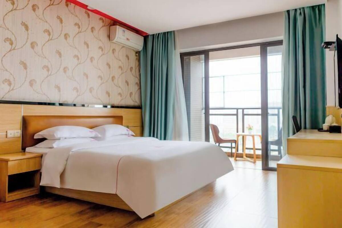 A hotel room with a bed, wooden headboard, a nightstand, a desk, and a chair.