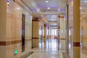 Un pasillo de hotel con piso brillante, puertas a los lados y un extintor de incendios a la derecha.