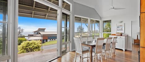 A spacious dining area with a large table and chairs, large windows with a view of the outdoors, and a ceiling fan.