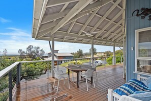 Une terrasse extérieure couverte, dotée d’une table et de chaises, qui offre une vue sur un quartier résidentiel.