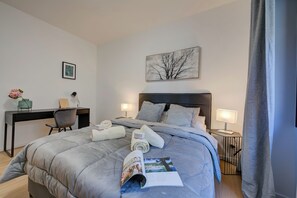Relax in a serene space with a neatly made bed, desk, and comfortable seating area.