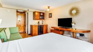 Ein Hotelzimmer mit Bett, Schreibtisch, Fernseher, einer Küchenzeile und einem grünen Sofa.
