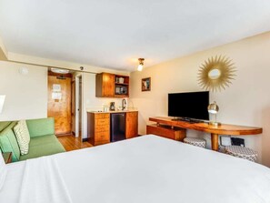 Una habitación de hotel con cama, escritorio, televisor, kitchenette y sofá verde.