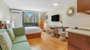 Moderni hotellihuone, jossa on sänky, vihreä sohva, ruokapöytä ja televisio.