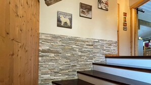 A staircase with a stone wall and wooden paneling, leading to a room with a door and framed pictures on the wall. - Attic Apartment 3 Rooms 74m², South Balcony, Private Parking, Wifi (La Clusaz)