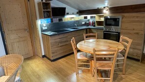 A compact kitchen with wooden cabinets, a built-in oven, a microwave, and a dining table with chairs. - Attic Apartment 3 Rooms 74m², South Balcony, Private Parking, Wifi (La Clusaz)