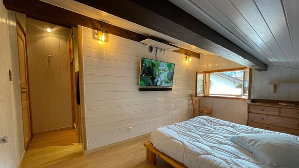 A bedroom with a bed, a television mounted on the wall, a window, and a wooden dresser. - Attic Apartment 3 Rooms 74m², South Balcony, Private Parking, Wifi (La Clusaz)