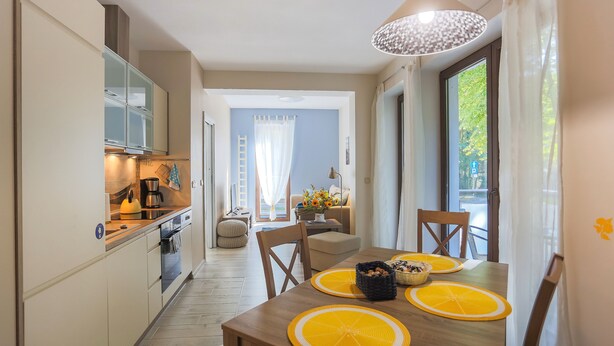 Una cocina moderna con comedor, que cuenta con una mesa de madera con individuales anaranjados, una lámpara colgante y vistas al exterior a través de una ventana.