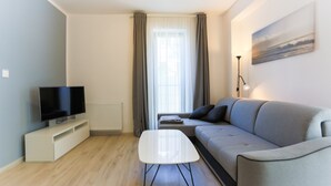 Una sala de estar moderna con un televisor de pantalla plana, un sofá gris, una mesa de centro blanca y una lámpara de pie.