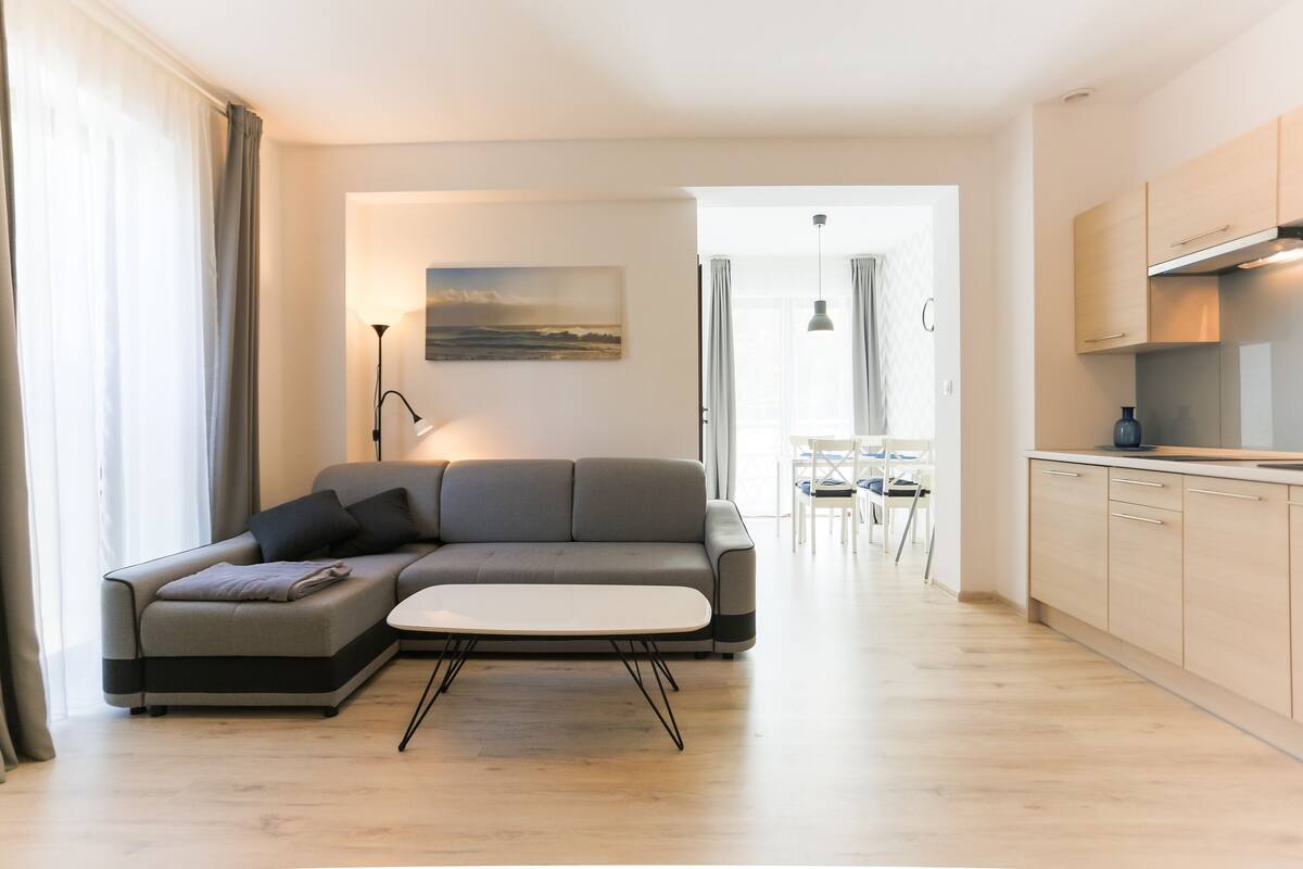 Een moderne woonkamer met een grijze bank, een klein wit tafeltje en een schilderij aan de muur.