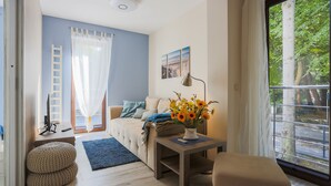 Una sala de estar moderna con un sofá, una mesa de centro con un jarrón de flores, una escalera y un ventanal con vistas a árboles.
