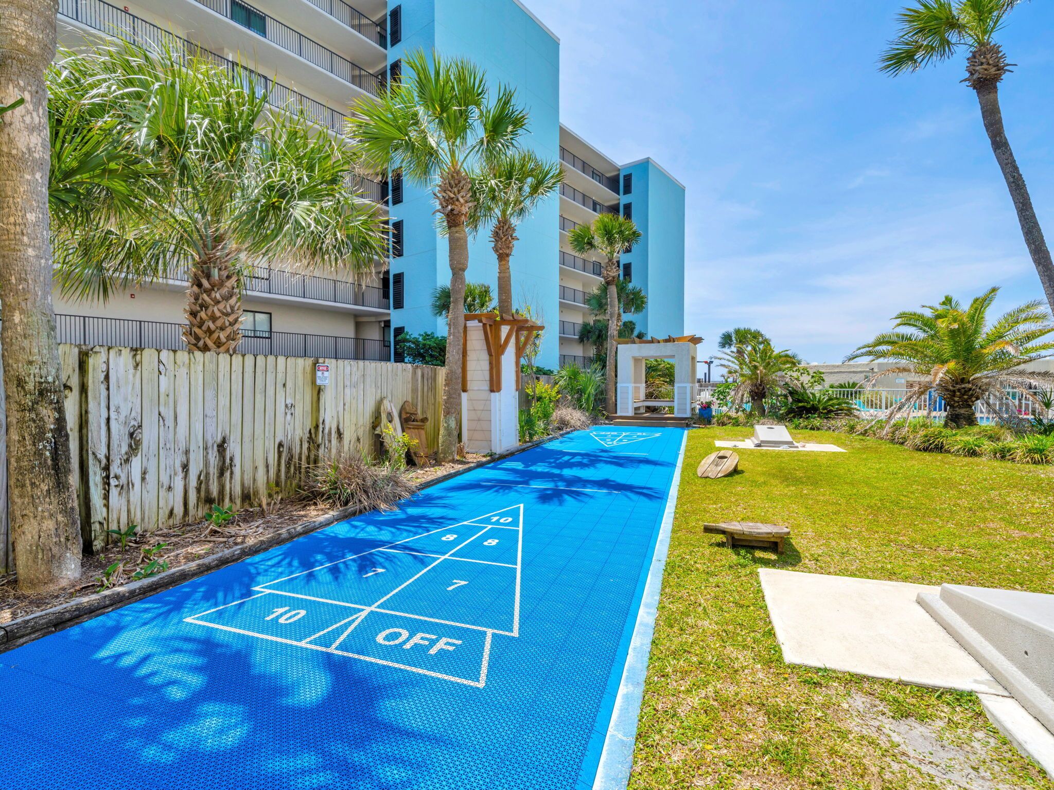 A pool area with a shuffleboard court, palm trees, and a wooden fence.