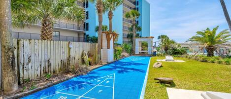 A pool area with a shuffleboard court, palm trees, and a wooden fence.