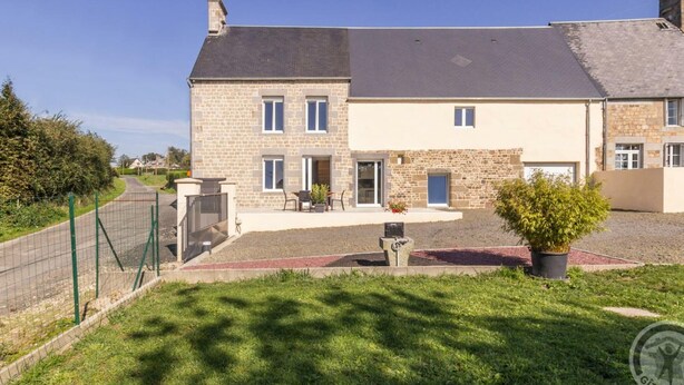 A two-story stone house with a paved driveway and a small patio area. - Charming family house with terrace in Normandy (Beslon)