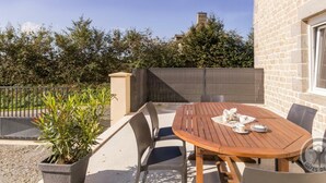 An outdoor patio with a round wooden table, four chairs, and a potted plant. - Charming family house with terrace in Normandy (Beslon)