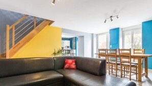 A modern living room with a black leather sofa, a wooden dining table with chairs, a staircase, and a kitchen area in the background. - Charming family house with terrace in Normandy (Beslon)