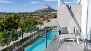 Ein Balkon mit Glasgeländer, der auf einen Swimmingpool blickt, mit einem weißen Sofa und einem kleinen Tisch.