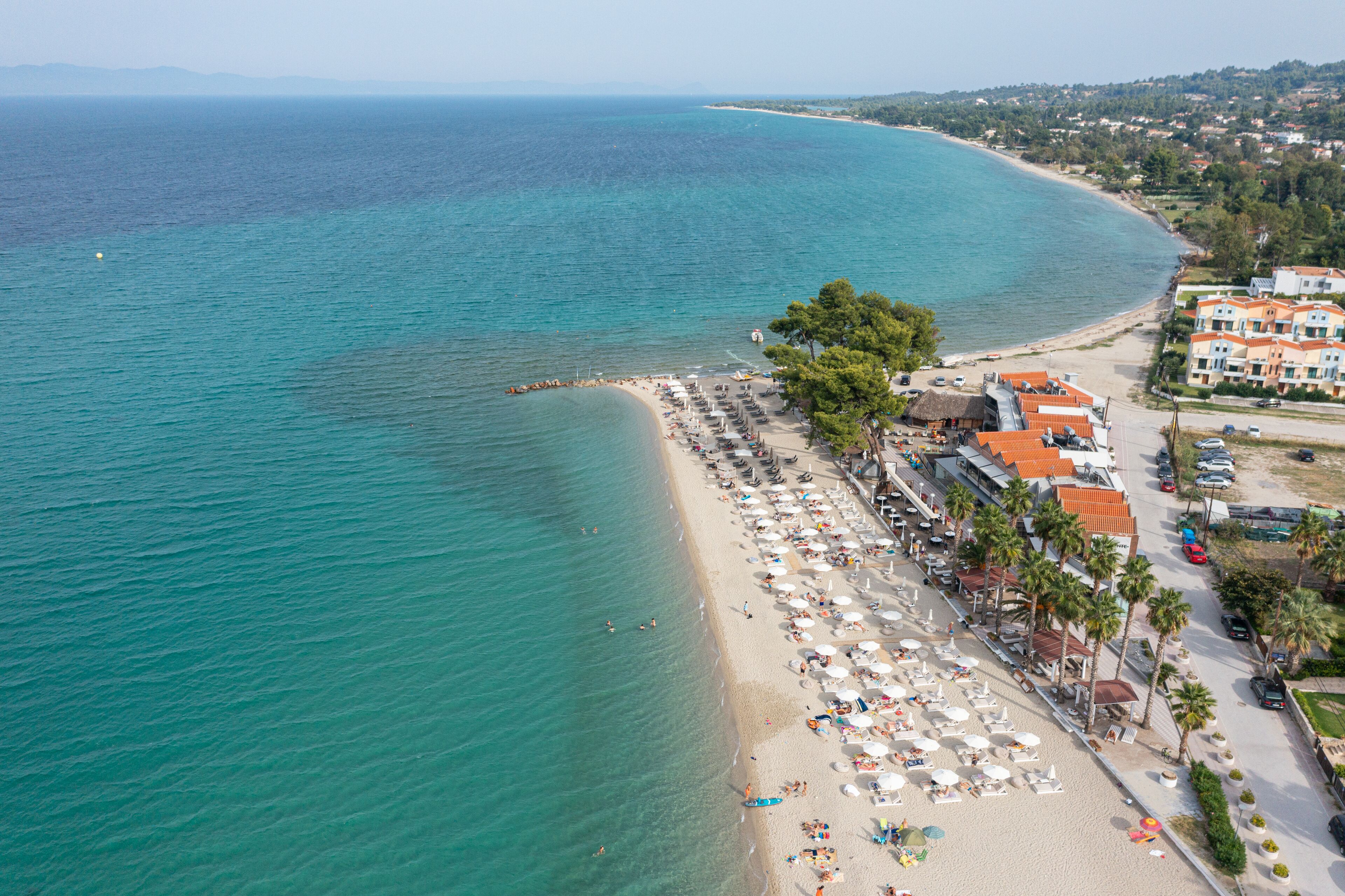An aerial view of a beach with a row of villas, a sandy beach, and clear turquoise waters.