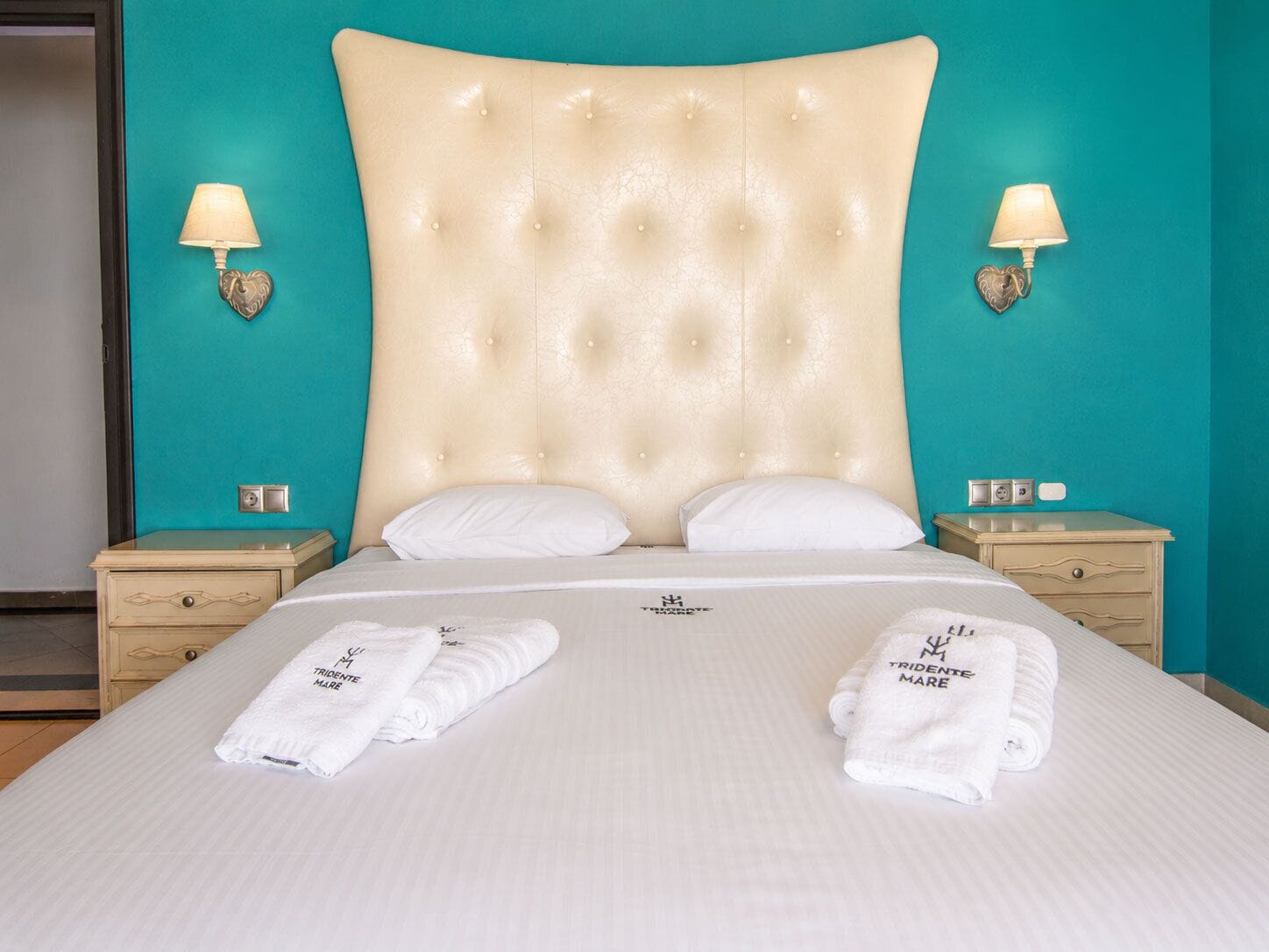 A large bed with a tufted headboard, two bedside tables, and two wall-mounted lamps.