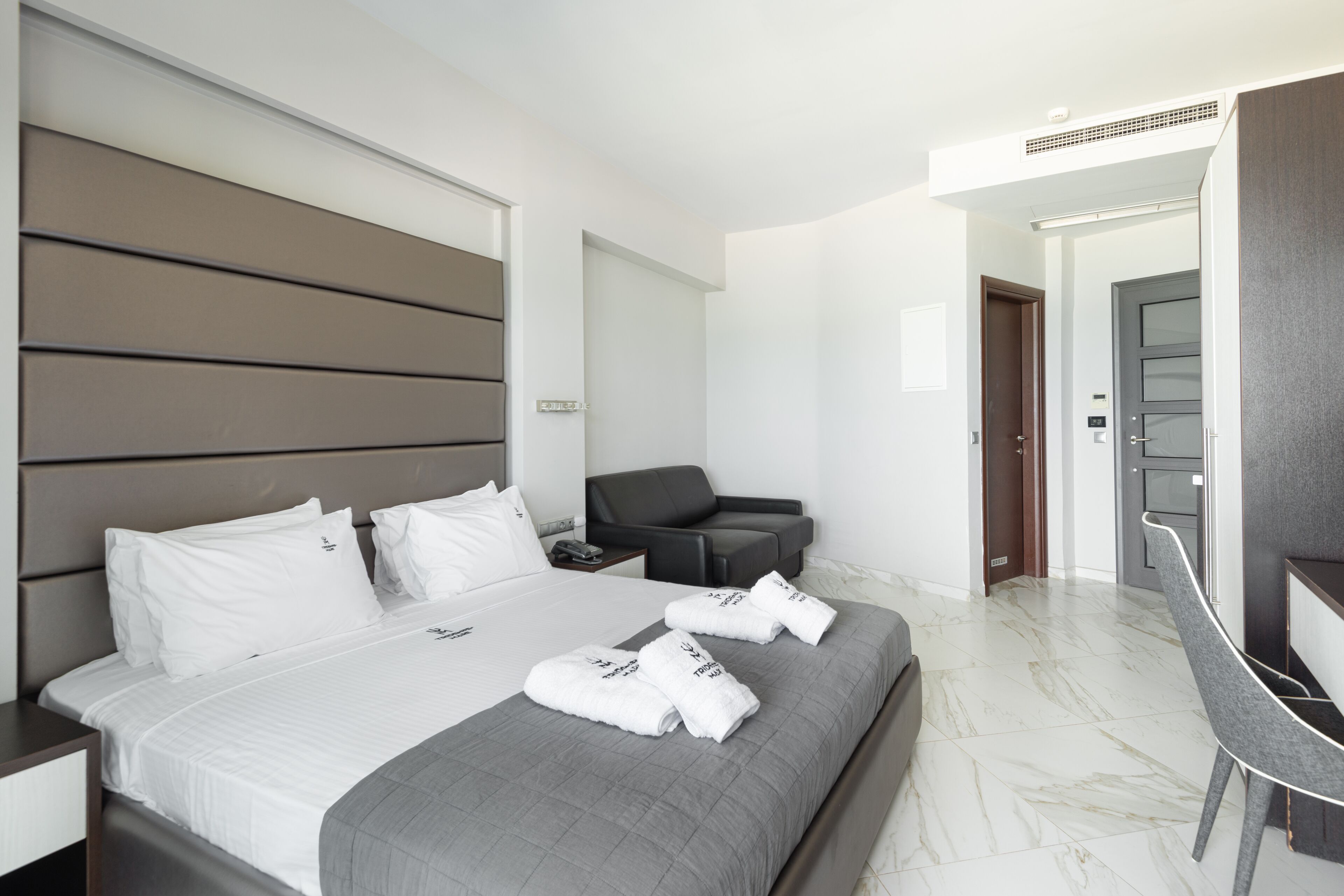 A modern hotel room with a large bed, a desk, a chair, and a bathroom door.