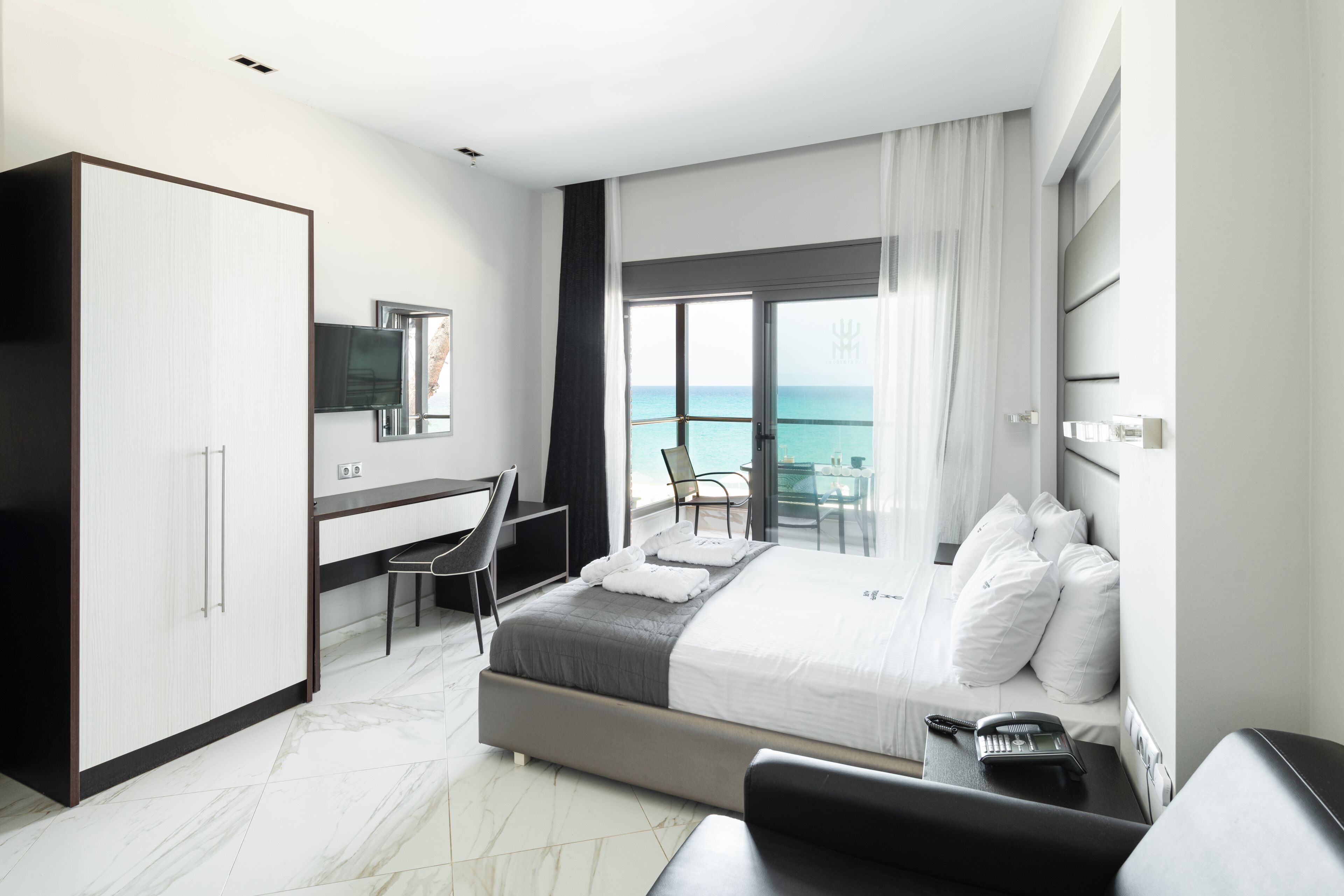 Une chambre d’hôtel moderne dotée d’un grand lit, d’un bureau, d’une chaise et offrant une vue sur la mer.