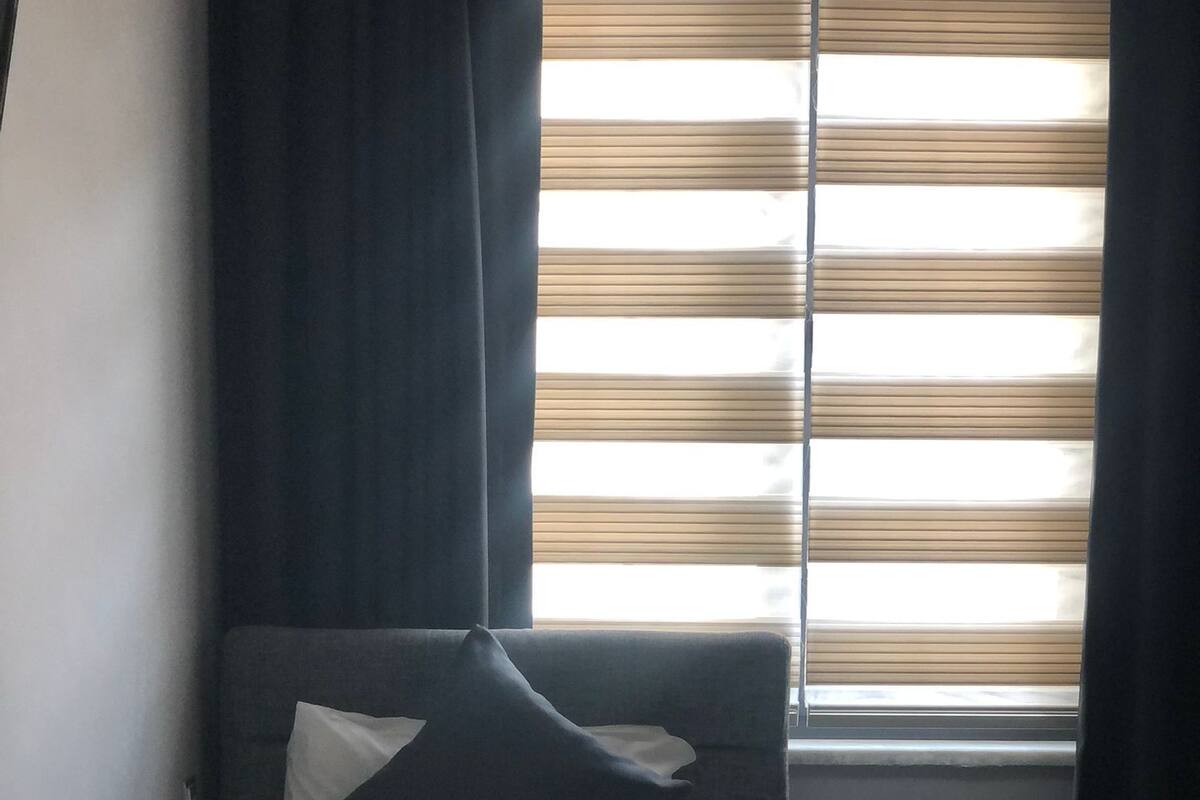 A neatly made bed with a white and black duvet, a dark blue pillow, and a small bedside table with a bottle and a tissue box.