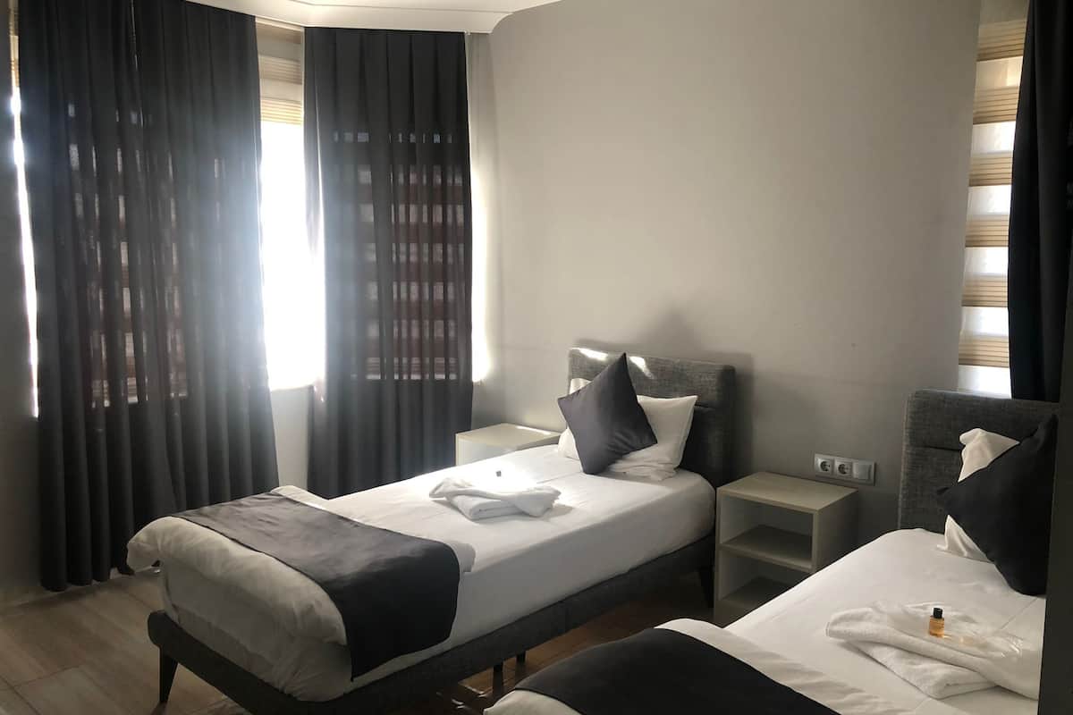 A hotel room with two beds, a bedside table, a nightstand, and a window with curtains.