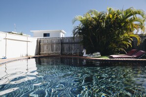 Una piscina cristalina con una valla de madera y un edificio blanco al fondo.