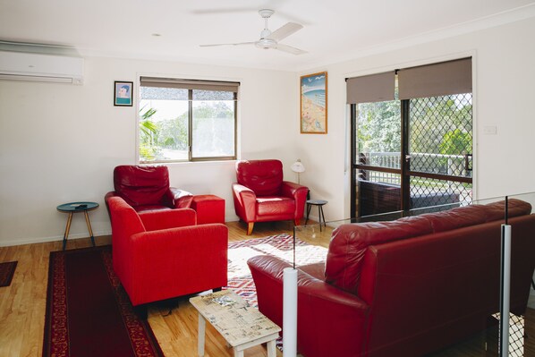 Una sala de estar con un sofá rojo, un sillón rojo, una mesita y un ventilador de techo.