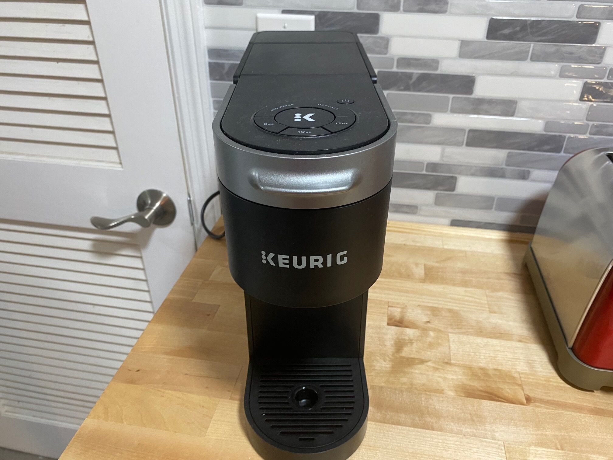 A Keurig coffee maker on a wooden countertop with a tiled backsplash in the background.