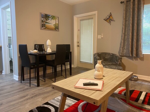 A dining area with a wooden table, black chairs, a painting of a beach scene, and a butterfly decoration on the wall.