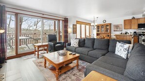 A spacious living area with a large sofa, a dining table, and a kitchen in the background. - Hauts-Bois Ski In/Out 2brs w/Pool Access (197-9) (Mont-Tremblant)