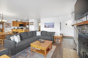 Un salon moderne avec un canapé d’angle gris, une table basse en bois et une cheminée en pierre.