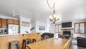 A modern kitchen with wooden cabinets, a stainless steel refrigerator, and a bar area with stools. - Hauts-Bois Ski In/Out 2brs w/Pool Access (197-9) (Mont-Tremblant)