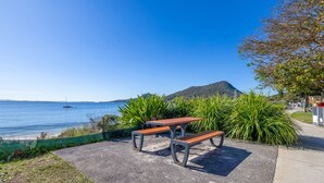 Uma área com bancos à beira-mar, com vista para o oceano e uma montanha ao longe.
