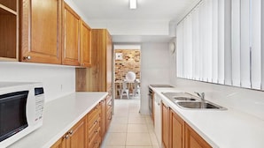 Cozinha moderna com armários de madeira, bancada branca e micro-ondas embutido.