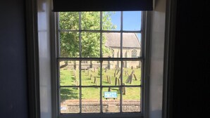 Ein Fenster mit Blick auf einen Friedhof und ein Gebäude mit einem Strohdach.