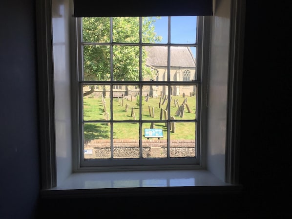 A window with a view of a cemetery and a building with a thatched roof. - Stylish Historic Apartment - Sleeps 3 & Parking (Norwich)