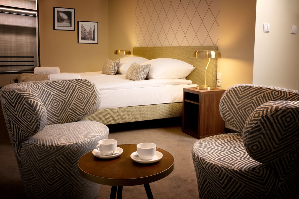 A hotel room with a bed, two armchairs, a small table with cups, and a lamp.