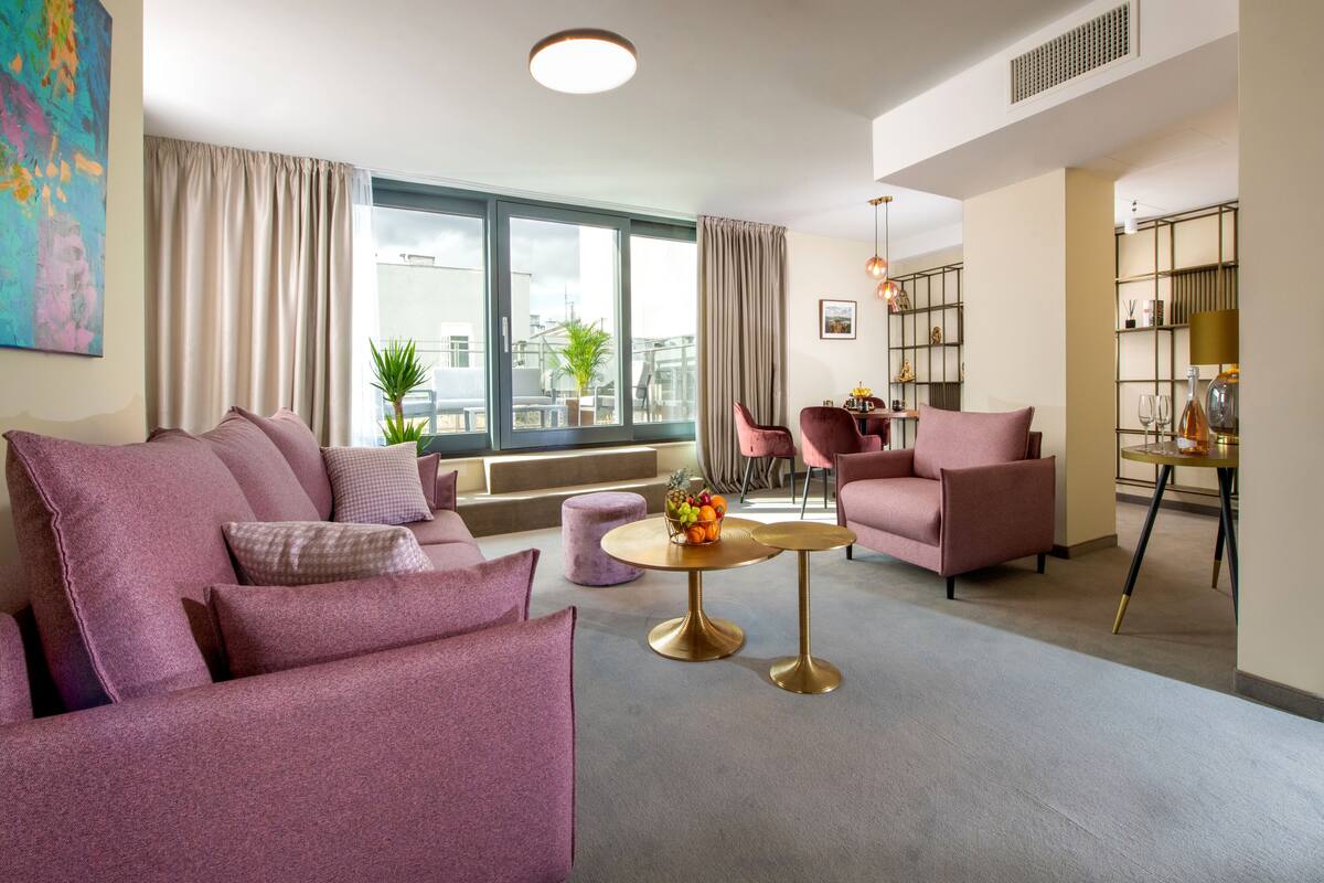 A modern living room with a sofa, armchairs, a round table, and a bookshelf.