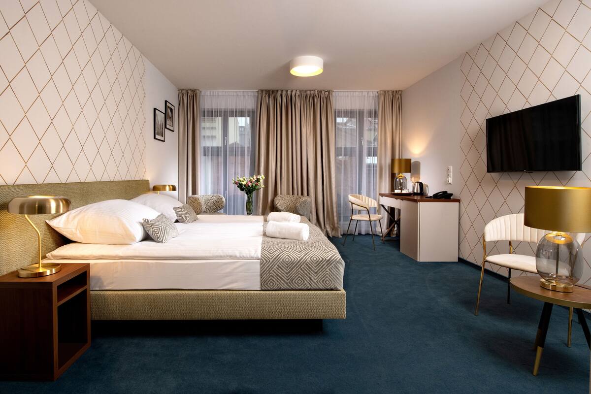 A hotel room with a large bed, a desk, a chair, and a TV.
