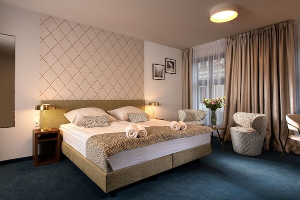 Une chambre d’hôtel avec un grand lit, deux tables de chevet avec des lampes, une chaise, une petite table avec un vase de fleurs et une fenêtre avec des rideaux.