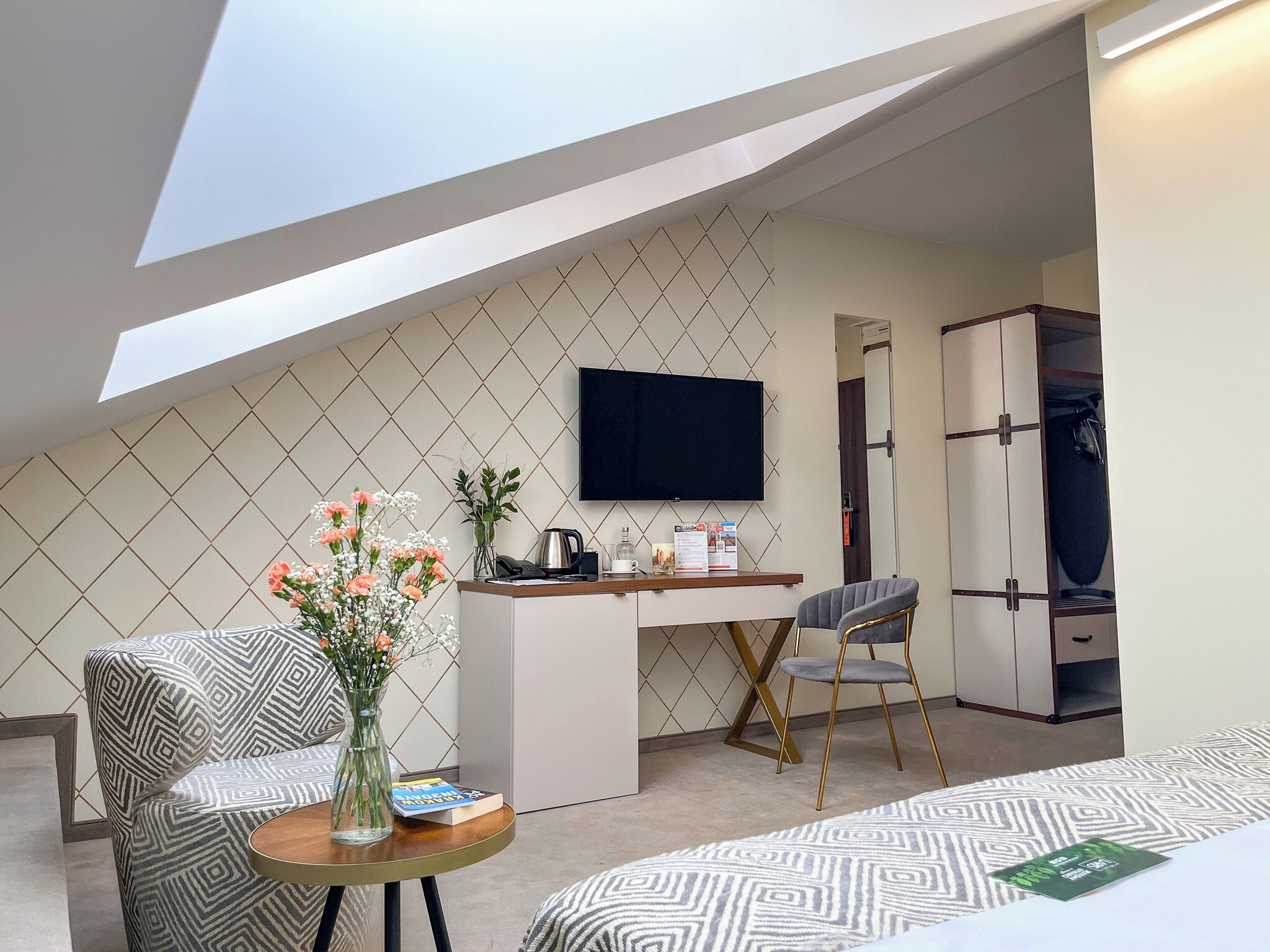 Une chambre d’hôtel moderne avec un lit en mezzanine, un bureau, une télévision et un coin salon doté de meubles à motifs.