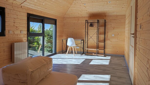 A modern interior with wooden walls, a large window, a white chair, a small table, and a bed.