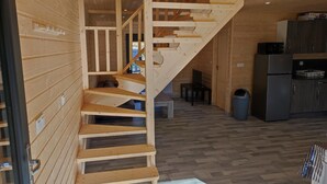 A wooden interior with a staircase leading to a loft area, a kitchen with a refrigerator, and a trash bin.