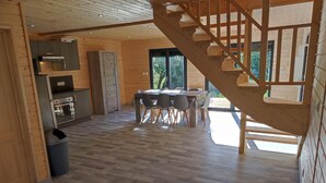 A spacious wooden interior with a dining area, kitchen, and a staircase leading to an upper level.