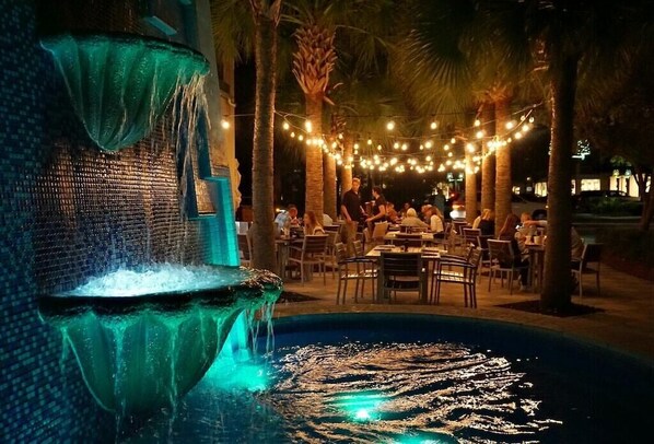 An outdoor dining area with string lights and palm trees.