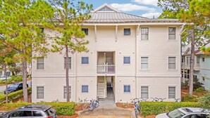 Un edificio residencial de varios pisos con una escalera central, un balcón en el segundo piso y un estacionamiento con bicicletas.